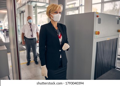 Elegant Businesswoman In Protective Medical Mask Passing Through Check-in Gate While Male Airport Worker Standing Behind Her