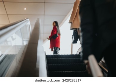 Elegant businesswoman in a red coat followed by a colleague on an escalator, ascending within a contemporary corporate setting. - Powered by Shutterstock