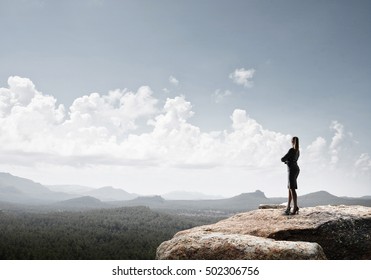 Elegant businesswoman standing on rock top and looking ahead