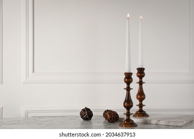 Elegant candlesticks with burning candles on white marble table. Space for text