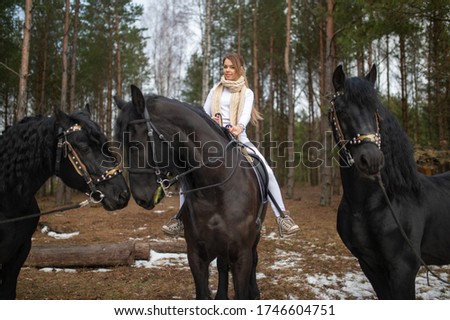 Elegant caucasian female in a grey coat riding on a black horse