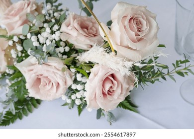 Elegant centerpiece set up on a dinner table, floral arrangement featuring soft blush-pink roses complemented by springs of greenery and white filler flowers, ethereal bouquet prepared for a wedding - Powered by Shutterstock