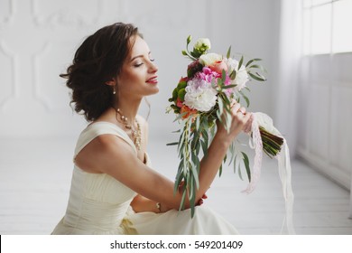 Elegant charming young brunette bride is sitting on white rustic wooden floor in a wedding dress with a big bouquet of flowers, daydreaming,  in the interior Waiting for groom. - Powered by Shutterstock