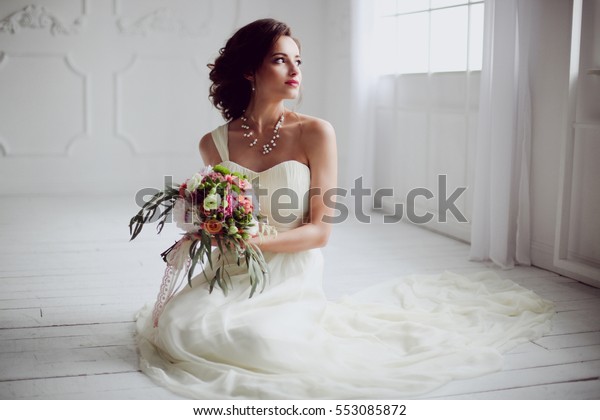 優雅な若いブルネットの花嫁が 白い田舎の木の床に 大きな花束の花束を持つ 白い背景に座り 空想的に 室内に花婿を待つ 詳細な修正 の写真素材 今すぐ編集