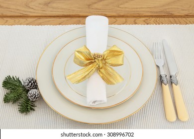 Elegant Christmas Dinner Place Setting With Plates, Antique Cutlery, Napkin And Gold Bow Over Silver Table Runner And Oak.