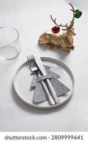 An elegant Christmas table setting featuring shiny cutlery, cloth napkins, fine plateware, and a charming golden reindeer figurine decoration.