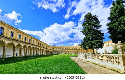 Elegant classical building with colonnade encircling lush green lawn, set against bright blue sky with white clouds, showcasing architectural beauty and natural serenity - Powered by Shutterstock