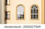 Elegant classical building facade with symmetrical arched windows, sunlit yellow wall, and decorative architectural details showcasing vintage European style and historic heritage architecture