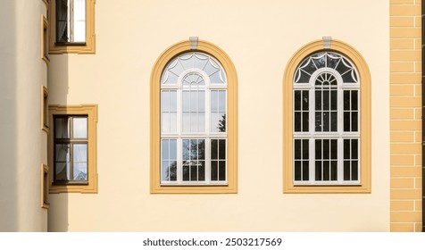 Elegant classical building facade with symmetrical arched windows, sunlit yellow wall, and decorative architectural details showcasing vintage European style and historic heritage architecture - Powered by Shutterstock