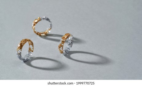 Elegant clear resin rings with half golden and silver filling standing on gray background, widescreen. Jewelry fashion photography