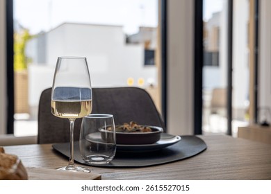 Elegant close-up of a dining table setting with a glass of white wine and a meal in the background.