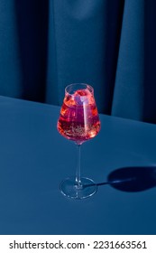 Elegant cocktail with red vermouth on blue background with shadow. Vermouth cocktail on coloured background in trendy style. Contemporary concept with alcohol beverage. Bartender cocktail
