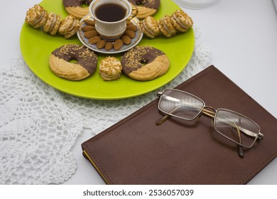 Elegant coffee cup with almond garnish, chocolate-covered cookies, and glasses resting on a leather notebook. Pink roses and a lantern create a cozy vintage vibe. - Powered by Shutterstock