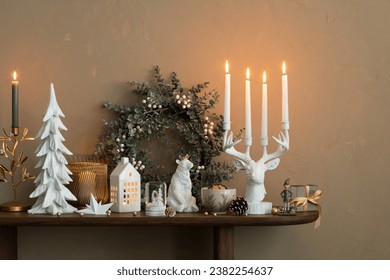 Elegant composition of christmas living room interior with wooden console, stylish wreath, deer candlestick with candle, clock, christmas tree, gifts and personal accessories. Home decor. Template.	
