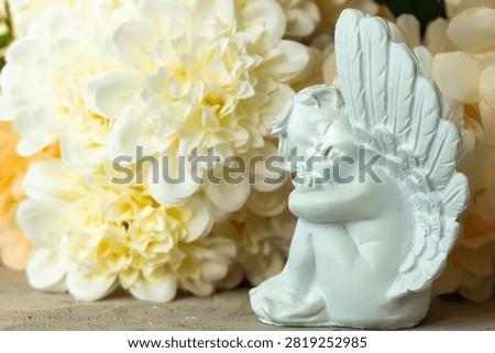 Elegant composition featuring a graceful sculpture of a small baby angel with a daydreaming, contemplative expression, against a soft pastel floral background. This elegant image is highly versatile and can be used for the following occasions: Valentine’s Day, Anniversaries, Sympathy, Memorials, 