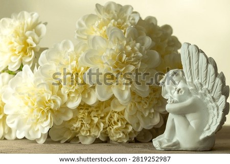 Elegant composition featuring a graceful sculpture of a small baby angel with a daydreaming, contemplative expression, against a soft pastel floral background. This elegant image is highly versatile and can be used for the following occasions: Valentine’s Day, Anniversaries, Sympathy, Memorials, 
