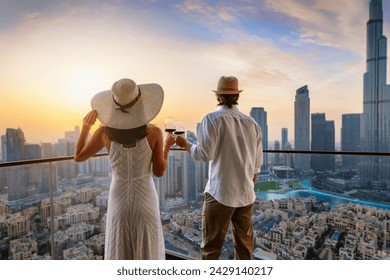 A elegant couple stands on a balcony and enjoys the sunset behind the skyline of Dubai with a drink in their hands - Powered by Shutterstock