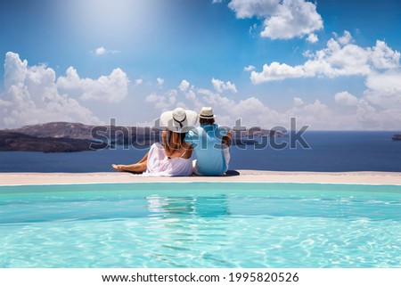A elegant couple in summer clothes sits by the pool and enjoys the view to the mediterranean sea in Greece during their summer holidays