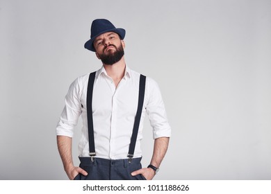 Elegant criminal. Handsome young man in suspenders keeping hands in pockets looking at camera while standing against grey background