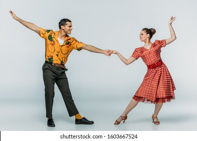 elegant dancers holding hands while dancing boogie-woogie on grey background