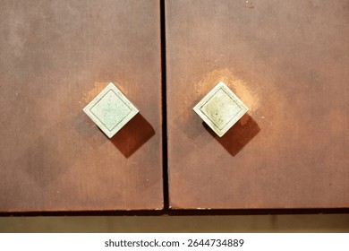 Elegant diamond-shaped door handles on brown wooden cabinet doors creating symmetrical design. Perfect for interior design, furniture, home decor, and architectural detail projects.
