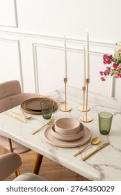 Elegant dining setup with marble table, gold cutlery, pink and green dishware, tall candles, and floral decor in a modern setting.