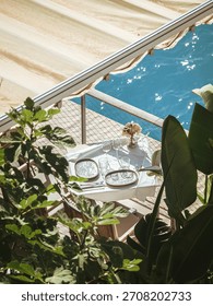 Elegant dining table set under a canopy on a seaside terrace in Nice, France, surrounded by lush greenery and overlooking the sparkling blue Mediterranean Sea.