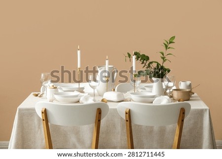 Elegant dining table set with white dinnerware, lit candles, and green foliage for a special occasion