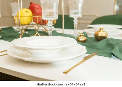 Elegant dining table setting with white ceramic plate and golden cutlery. Festive serveware decor in luxury kitchen interior. Modern lifestyle concept for restaurant or home celebration.