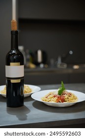 An elegant dinner setup featuring a bottle of wine and plates of pasta topped with tomato sauce and basil in a modern kitchen setting.