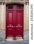 Elegant double red doors with ornate panels and brass details, set in a stone facade. The vibrant color contrasts with the neutral stone, creating a striking entrance. Classic architectural design wit