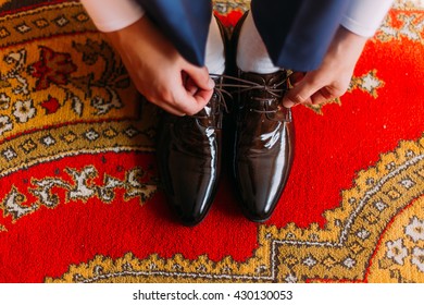 Elegant Dressed Man Tying Stylish Leather Shoes Indoors Standing On Fancy Oriental Style Carpet