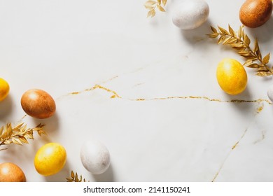 Elegant Easter background. Frame made of luxury Easter eggs and golden branches on marble table. Flat lay, top view, copy space.