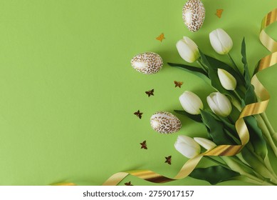 Elegant Easter composition featuring decorated eggs, white tulips, butterfiles confetti and a soft ribbon arranged on a bright green background
