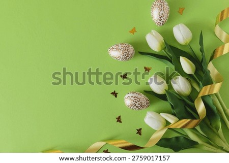 Elegant Easter composition featuring decorated eggs, white tulips, butterfiles confetti and a soft ribbon arranged on a bright green background