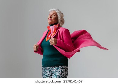 Elegant elderly woman looking like super hero while wearing pink coat against grey background - Powered by Shutterstock