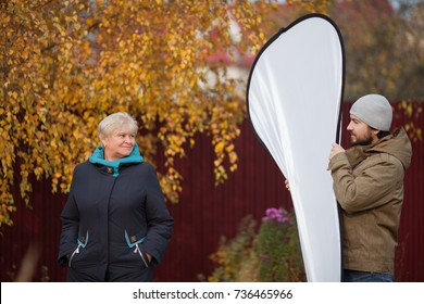 Elegant Elderly Woman Posing To Photographer, Assistant Holding Reflector, Natural Light Photography, Process Of Photosession, Autumn Day, Cold Weather