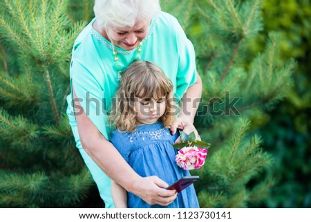Elegant elderly woman, taking selfie portrait with her granddaughter, smiling, teasing and making faces, having fun together, concept of elderly people and technology, family love