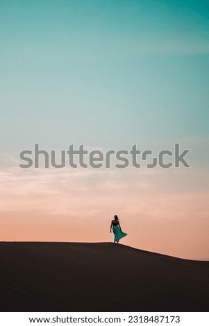 Elegant and ethereal, a woman in a blue skirt glides through a sand dune, a vision of grace amidst the textured desert backdrop
