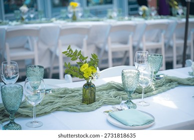 Elegant event dining table setup with sage green decor, vintage embossed glassware, and floral runner detail. Perfect for weddings and upscale celebrations.