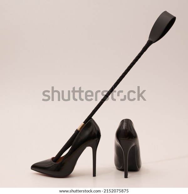 Elegant expensive black\
high heel women shoes with riding crop on white background - fetish\
female weapon