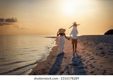 A elegant family in white clothing walks hand in hand down a tropical paradise beach during sunset tme and enjoys their summer vacatios - Powered by Shutterstock