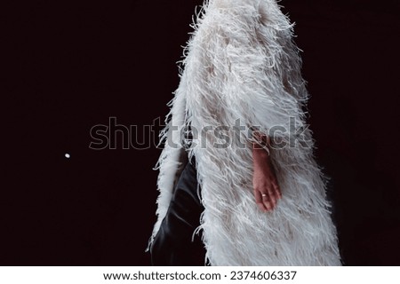 Elegant fashion details of Haute couture white ostrich feather coat. Fashion model walking on black background