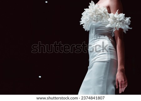 Elegant fashion details of white silky bridal dress. Fashion model walking on black background