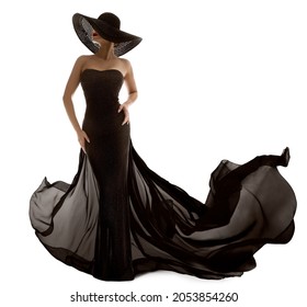 Elegant Fashion Model in Black Dress. Sexy Woman Silhouette in Hat. Luxury Lady in Long Evening Gown with Waving Fabric over White Background