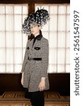 Elegant Fashion Statement - Chic Houndstooth Coat Paired with Bold Feathered Hat for a Sophisticated and Dramatic Style Ensemble.