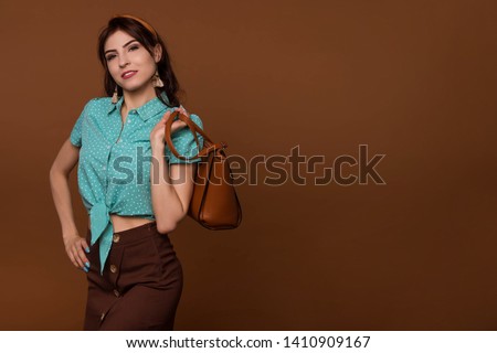 Elegant fashionable woman with leather handbag. Stylish pin-up girl holding brown bag. Female fashion vogue. Brown, coffee background. Copy space.