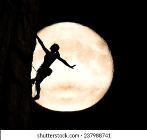 Elegant female extreme climber and big moon. Silhouette of female rock climber hanging on her hand on the vertical rock with big moon on the background