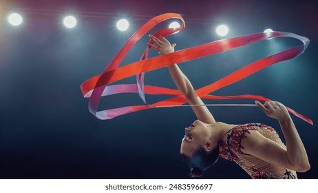 Elegant Female Gymnast in Stunning Backbend, Skillfully Twirling Vibrant Ribbon Under Bright Stadium Lights. Capturing Grace, Flexibility, and Precision in an Tournament Winning Gymnastics Performance - Powered by Shutterstock