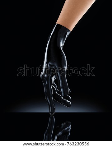 Elegant female hand in black latex glove on a black background. Female hand in liquid black oil or acrylic paint